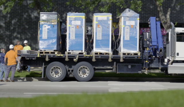 A flatbed truck delivering four large, shrink-wrapped commercial boilers for a massive high-rise HVAC upgrade and mechanical rigging project at Lake Point Tower in Chicago.