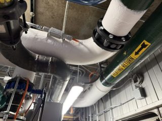 Chicago Commercial HVAC - Hydronic Heating Return Piping An overhead view showcasing masterful hydronic pipe work, featuring a clearly labeled heating return line and heavy-duty insulated piping inside the upgraded mechanical penthouse at Lake Point Tower.