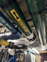 Chicago Commercial HVAC - Hydronic Heating Return Piping An overhead view showcasing masterful hydronic pipe work, featuring a clearly labeled heating return line and heavy-duty insulated piping inside the upgraded mechanical penthouse at Lake Point Tower.