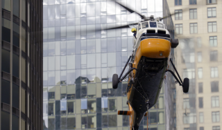 Chicago Commercial HVAC - High-Rise Helicopter Rigging Striking close-up view of a heavy-duty helicopter mid-flight against a modern glass high-rise, executing a complex commercial HVAC rooftop boiler lift at Lake Point Tower in Chicago.