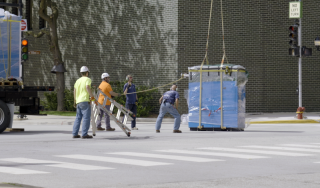 Chicago Commercial HVAC - Helicopter Boiler Lift-Off A heavy-duty helicopter lifts a massive, shrink-wrapped commercial boiler from a secured downtown staging area, kicking off a complex high-rise HVAC rigging operation at Lake Point Tower.