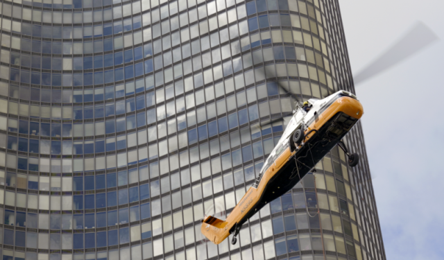 A heavy-duty commercial helicopter descending alongside the curved glass exterior of Lake Point Tower to retrieve the next boiler during a massive Chicago HVAC replacement project.