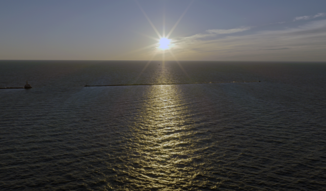 Expansive aerial view of the sun shining over Lake Michigan, highlighting Chicago's coastal environment, breakwater systems, and marine infrastructure.