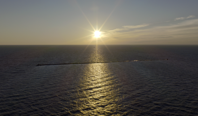 Wide aerial perspective of the sun rising over Lake Michigan with a prominent concrete breakwater, highlighting the coastal environment surrounding Chicago's commercial properties.