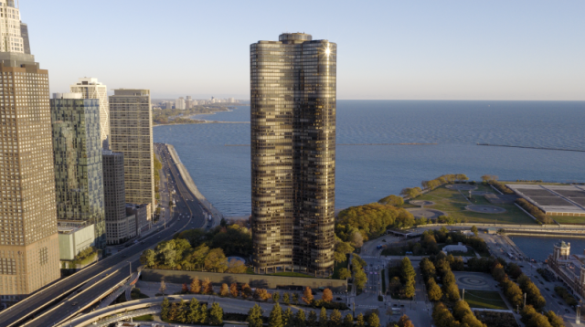 Wide aerial view of Lake Point Tower's curved glass facade reflecting the sunlight, set against Lake Michigan and Chicago's premier lakefront commercial infrastructure.