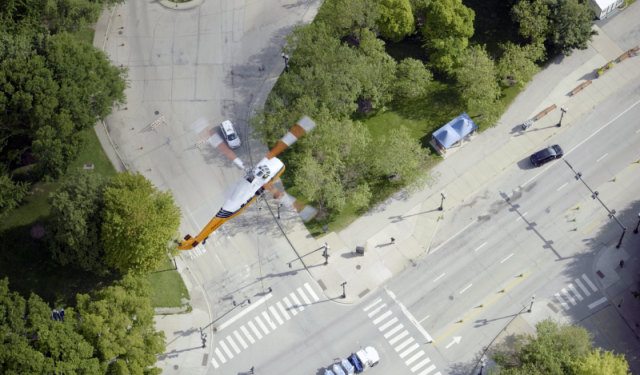 Top-down aerial view of a heavy-duty helicopter hovering over a closed downtown Chicago intersection, preparing to lift the first commercial boiler for a massive high-rise HVAC upgrade at Lake Point Tower.