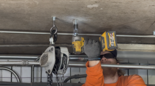 High-Rise Mechanical Installation - Hoist Anchor Prep High-rise mechanical room rigging featuring a technician installing eye-bolts for heavy equipment chain hoisting.