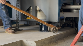 Commercial HVAC Installation - Equipment Pry Bar Lift Commercial HVAC technicians using a pry bar and machine rollers to position heavy equipment for a spring vibration isolator installation at Lake Point Tower.