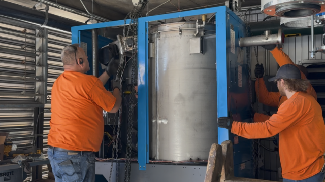 Commercial HVAC technicians using a chain hoist to lower a heavy P-K boiler into position during a high-rise mechanical installation at Lake Point Tower.