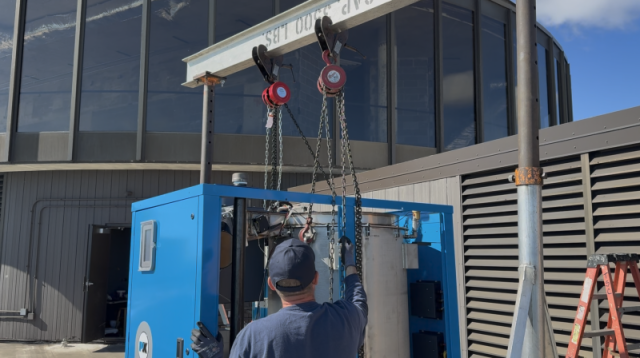High-rise commercial mechanical rigging featuring a gantry crane hoisting a new boiler unit.